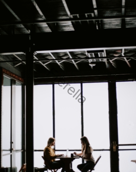 photo of two women facing each other sitting in front of table near glass wall