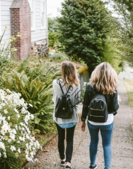 two ladies walking on sidewalk with black backpacks